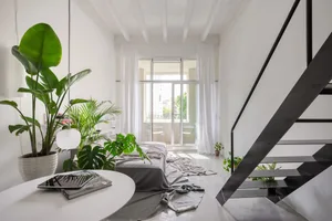 A minimalist living room with concrete walls, a black staircase, and large windows allowing natural light to filter in.