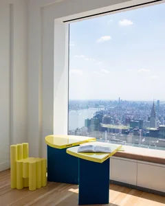 A modern interior featuring a glass desk with a cityscape view through a large window.