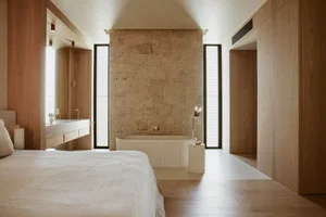 A minimalist bedroom with a large bed, a wooden floor, and a white plaster wall in the center.