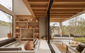 A modern minimalist living room with wooden elements, featuring a cozy seating area, a bookshelf filled with decorative items