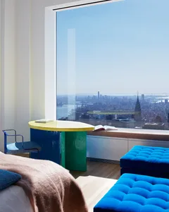 Interior view of a modern residential space featuring a glass table and blue upholstered stools with a large window overlooki