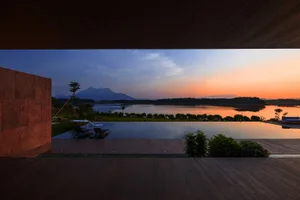 A serene waterfront villa featuring a wooden pool under a beautiful sunset.