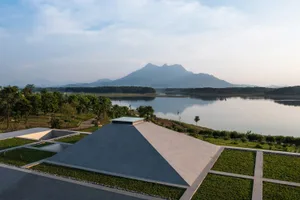 A minimalist concrete pavilion overlooking a serene lake with mountains in the background.
