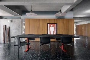 A modern dining room featuring a black granite dining table with black chairs and a concrete wall, accented by a wooden panel