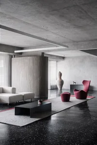 A modern minimalist living room with concrete walls, a terrazzo floor, and leather furniture and accents.