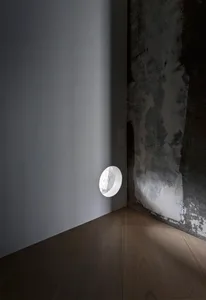 A minimalist space featuring a textured concrete wall, with a circular light source casting a shadow on the adjacent wall and