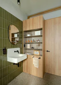 A modern bathroom featuring green tiles on the walls, wooden cabinets, and a white porcelain sink.