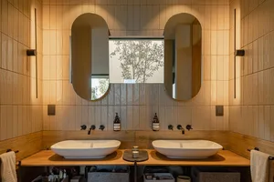 A modern bathroom with ceramic tile and wooden elements, featuring two sinks and a window.