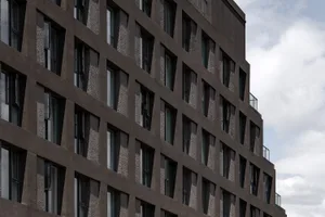 The exterior of a modern building with black concrete and textured panels, featuring numerous windows.