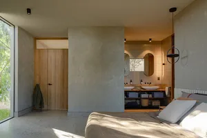 A minimalist bedroom with concrete walls, a bed, and a bathroom area in the background.