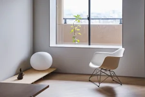 A minimalist living room featuring a white armchair, wooden floor, and large window with a view of the city.