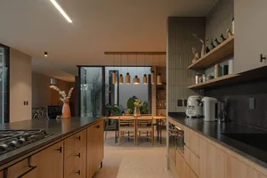 A modern residential kitchen featuring light wood cabinets and a stone countertop with pendant lights hanging above an island