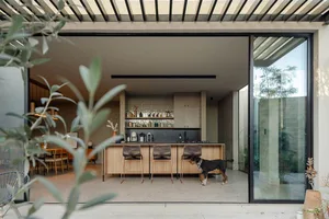 A modern residential interior with a wooden kitchen island, bar stools, and a dog in the foreground.