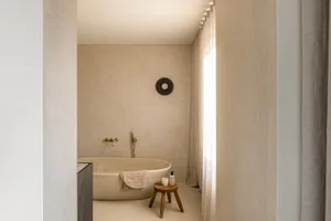 A minimalist bathroom with a concrete bathtub, golden faucet, and natural lighting.