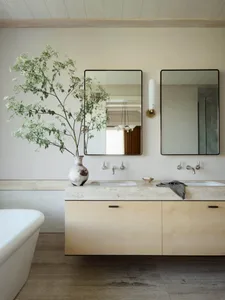 A modern bathroom featuring a floating wooden vanity counter with a stone countertop, dual sinks, and a large vase with green