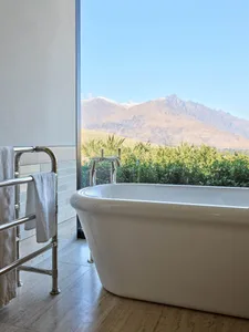 Modern bathroom featuring a white freestanding bathtub with metal fixtures, set against a scenic mountain backdrop.