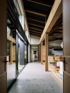Modern entrance hallway with wooden beams, glass walls, and concrete flooring.