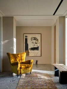 A modern interior design featuring a yellow upholstered armchair on a concrete floor, with a large abstract wall art piece.
