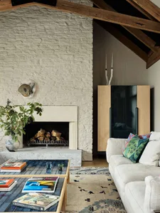 Modern living room featuring a comfortable sofa, a stone fireplace with wooden beams, and a coffee table with books and magaz