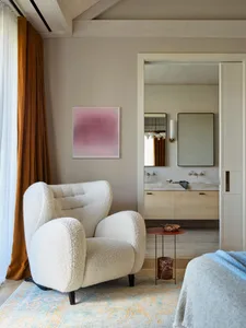 A modern living room featuring a comfortable white wingback chair with a traditional texture, a red side table, and a blue bl