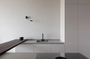 A minimalist modern kitchen featuring concrete countertops, stone backsplash, and a mixer sink.