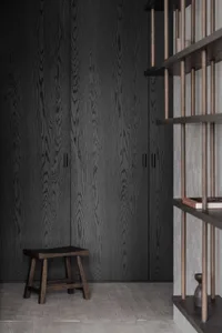 Modern storage space featuring black wooden cabinets with simple handles, wooden stool, and floating shelves with books and d