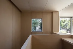 一間極簡風格的房間，擁有木質牆面與天花板，設有一扇小窗可眺望窗外綠意。