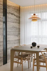 A modern dining room featuring marble walls and a concrete floor with a white table and wicker chairs.