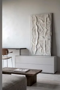 A minimalist living room featuring modern furniture and a concrete and wooden cabinet, with a textured wall piece and a woode