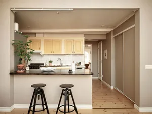 Minimalist residential kitchen with wooden flooring and cabinets, white countertops, and a sink with a potted plant.