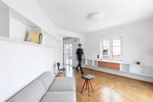 Minimalist living room with white walls, a gray sofa, and a wooden floor.