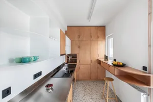A minimalist residential kitchen with wooden cabinets, stainless steel countertops, and a small dining nook.