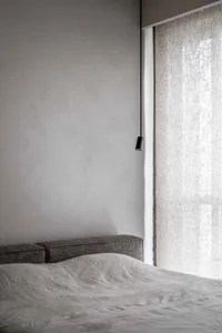 A modern grey bedroom featuring a bed draped in light grey fabric, minimalistic design, and natural light filtering through s