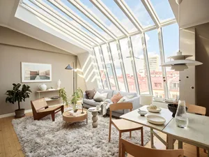 Modern living room featuring wooden furniture, glass windows, and light-colored upholstery.