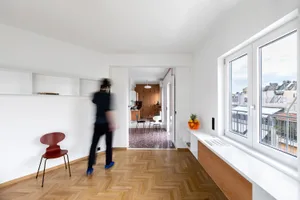 A modern living room featuring wooden flooring, minimalist furniture, and a large window overlooking the city.