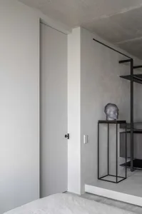 A minimalist bedroom featuring a concrete wall and floor, with a bed and a sculpture on a pedestal.
