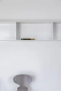 A minimalist white interior with a bookshelf and a chair.