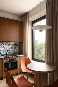 Modern kitchen with wooden cabinets, marble backsplash, round table, and orange chairs.