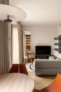 A modern living room with a library, featuring neutral-toned furniture and a large, round pendant light.