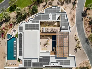 Aerial view of a modern residential building with white and black exterior, featuring solar panels and a swimming pool.
