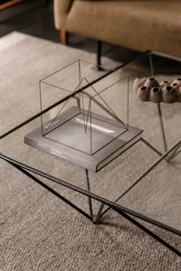 A minimalist metal frame sculpture on top of a book in a living room setting.