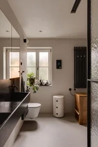 Modern bathroom with concrete floor, black sink, and white toilet, featuring a potted plant and minimalistic decor.