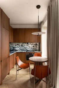 A modern kitchen with wooden cabinets, marble countertops, and metal chairs.