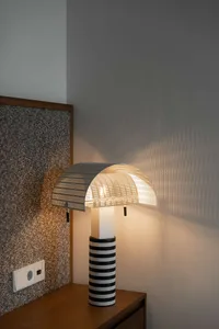 A modern lamp with a striped black and white base and a semi-transparent light shade, casting a warm glow on the adjacent wal