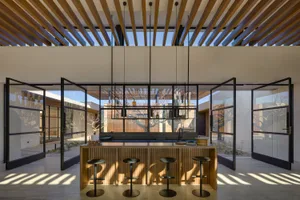 A modern residential kitchen with an open space layout, featuring a wood island and stools, under a wooden lattice ceiling wi