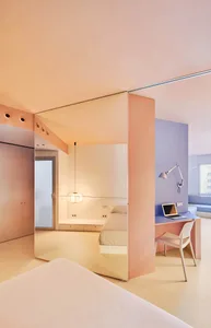 Minimalist bedroom with pink and white walls, a bed, and a desk with a laptop.