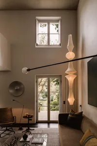 A minimalist living room featuring modern furniture, a large hanging lamp, and a view of the garden through the glass door an
