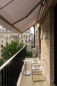 A modern balcony with brick walls and metal railings features two transparent chairs and a small table.