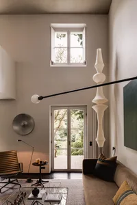 A modern interior design featuring a living room with neutral-toned furniture, a tall floor lamp, and a French door leading t