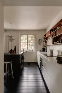 Modern minimalist kitchen with white cabinetry and wooden accents, featuring an island with pendant lighting and open shelvin